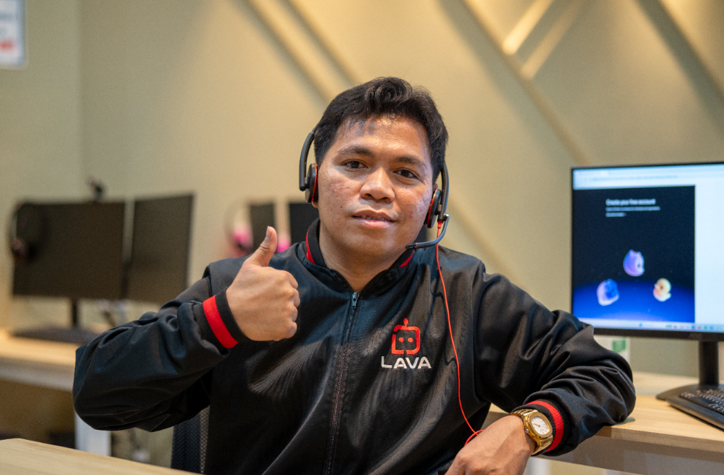 LAVA Automation team member wearing a headset and branded jacket, giving a thumbs up at his workstation.