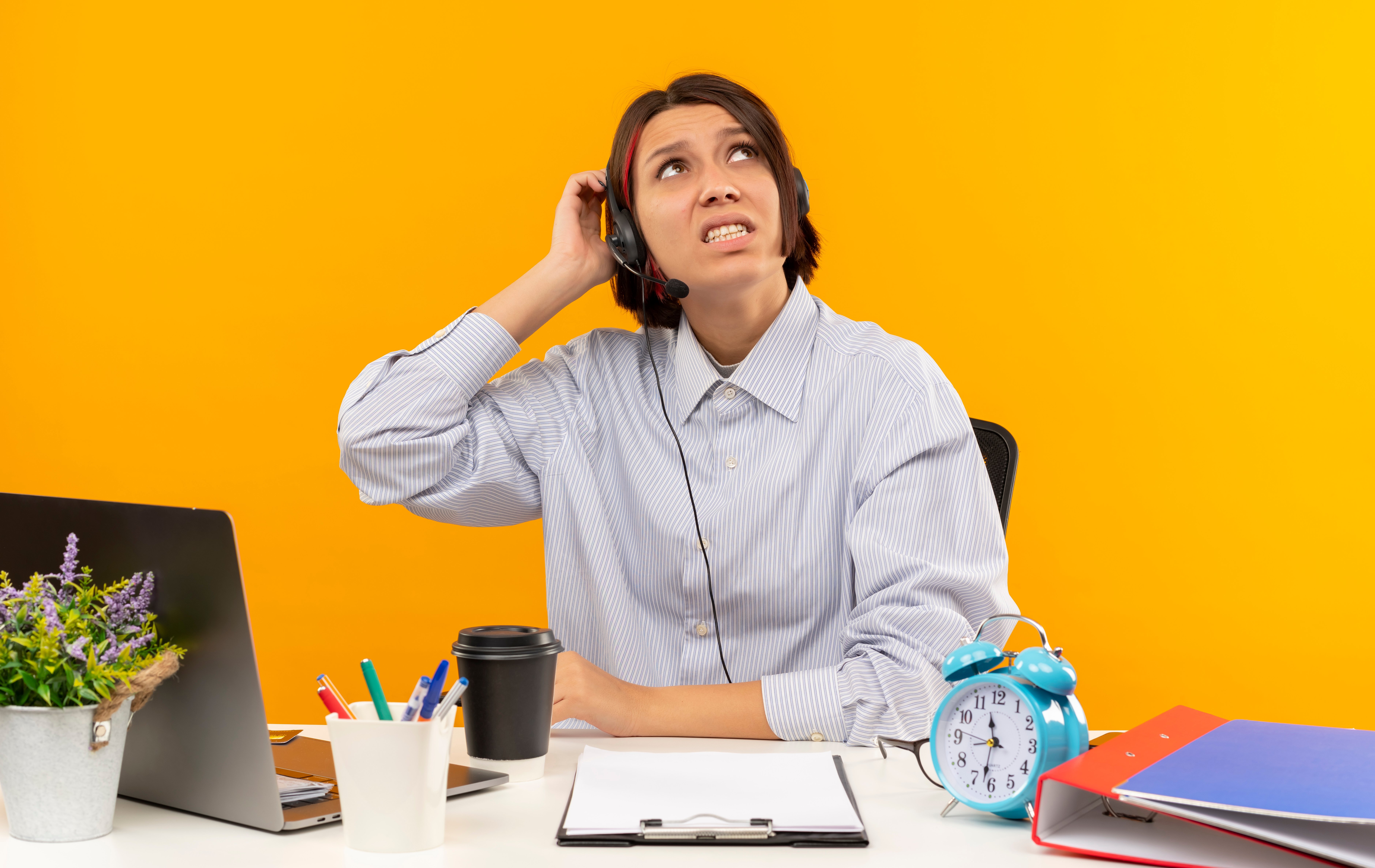 female virtual assistant wearing a headset sits at a desk, scratching her head and looking upward
