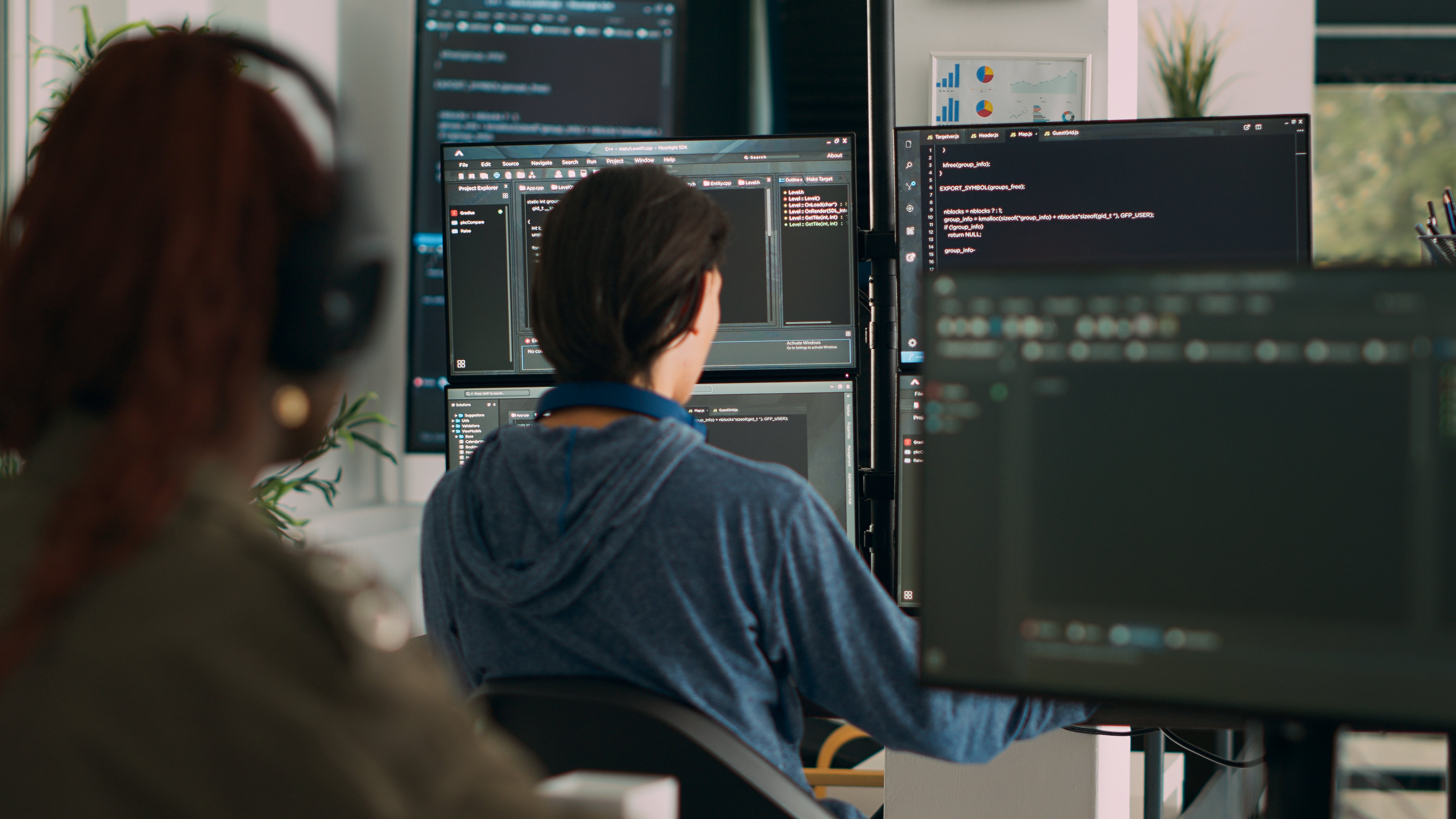 Two software developers working at a multi-monitor workstation displaying code