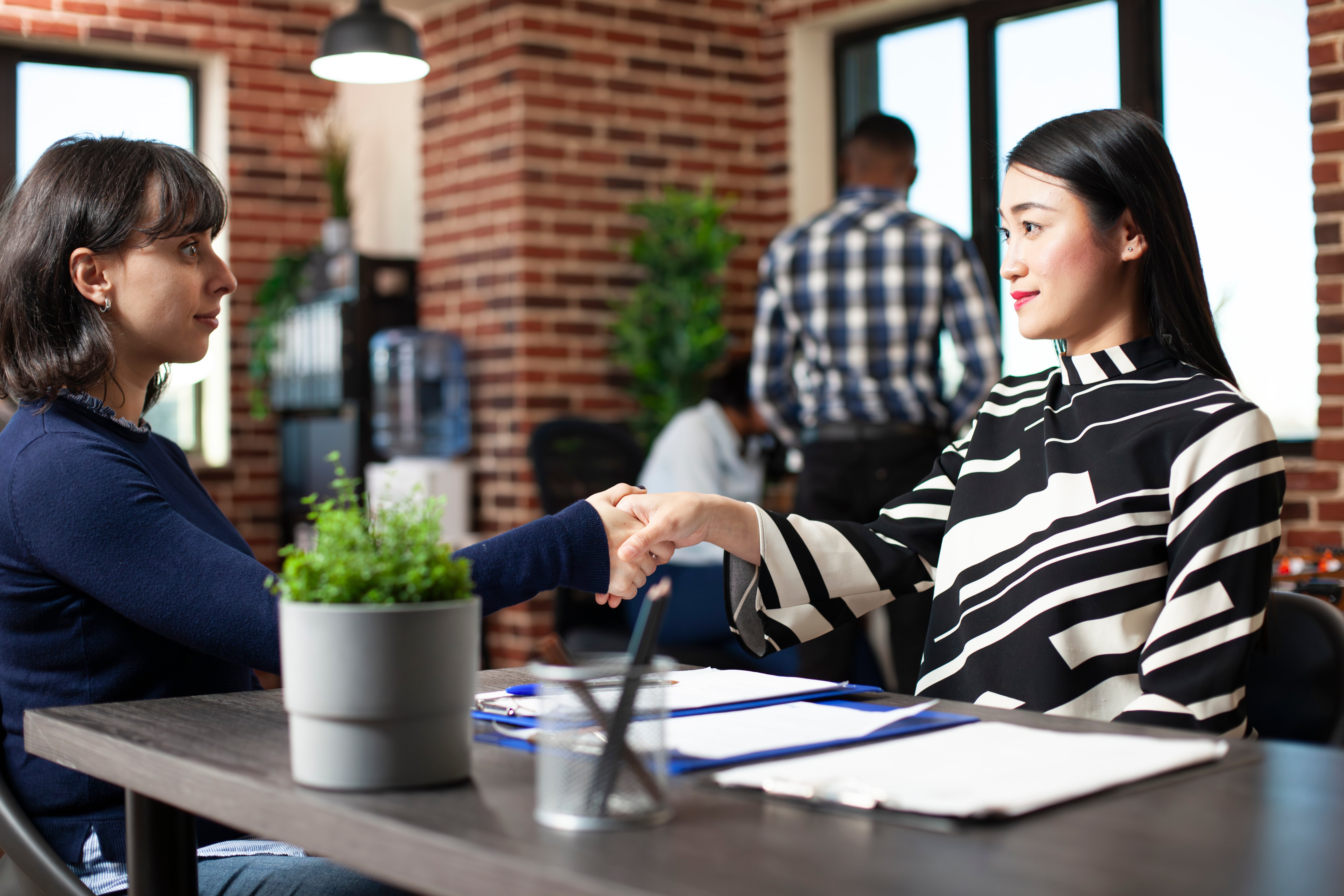 Two women shaking hands across a desk