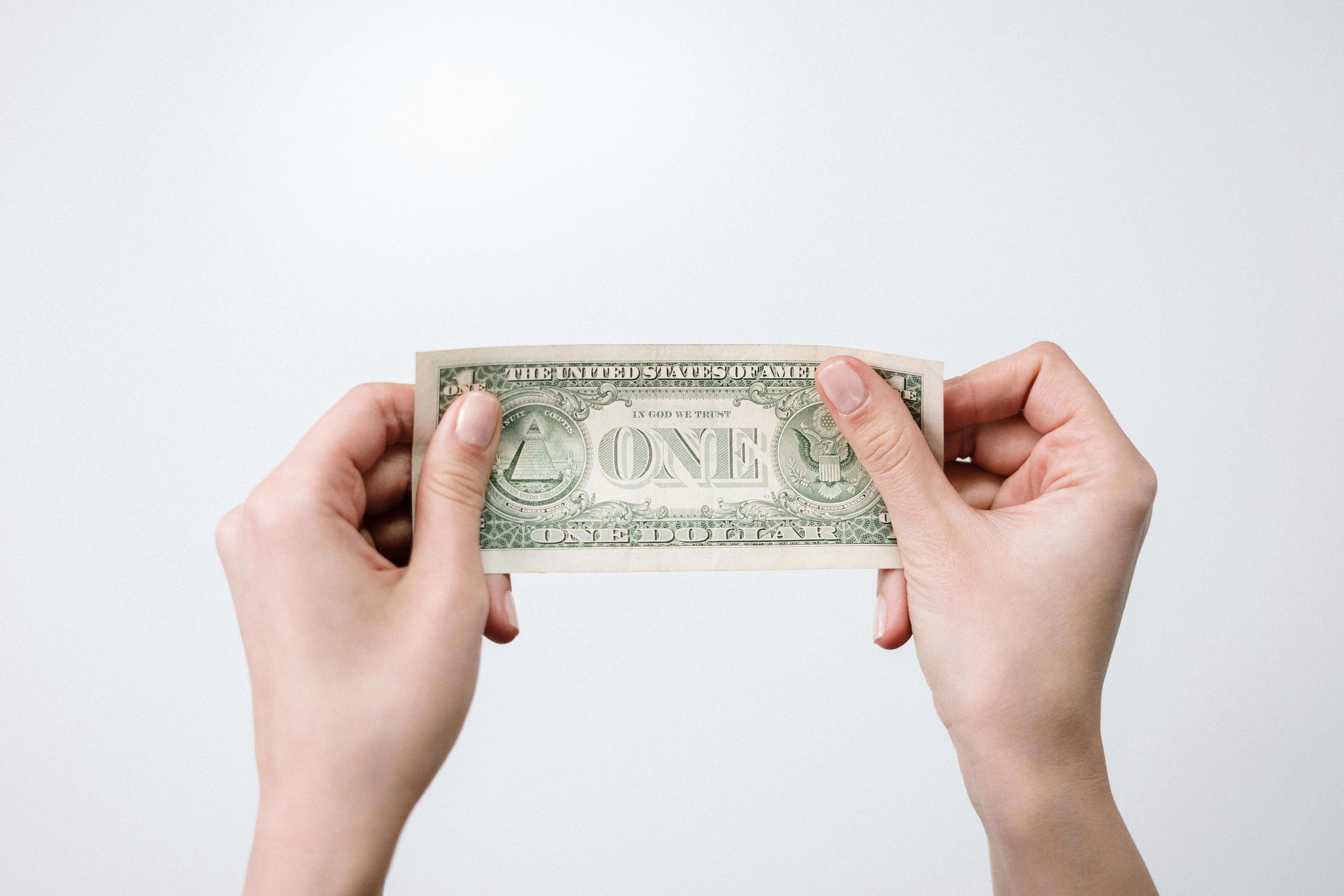 Two hands holding a US one-dollar bill by its edges against a light gray background.