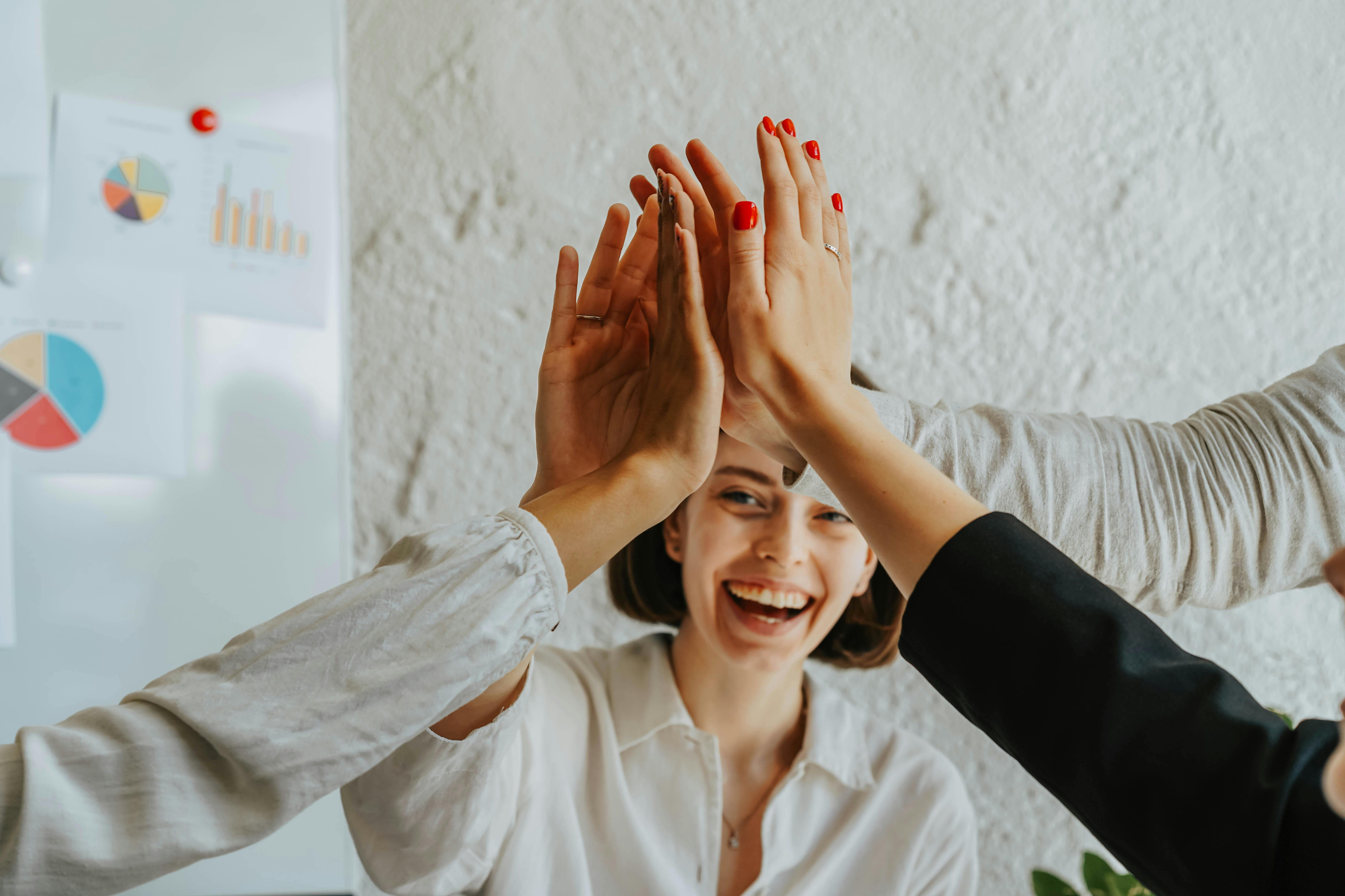 colleagues in a corporate setting share a high-five, with a smiling team member in front and business charts displayed in the background.