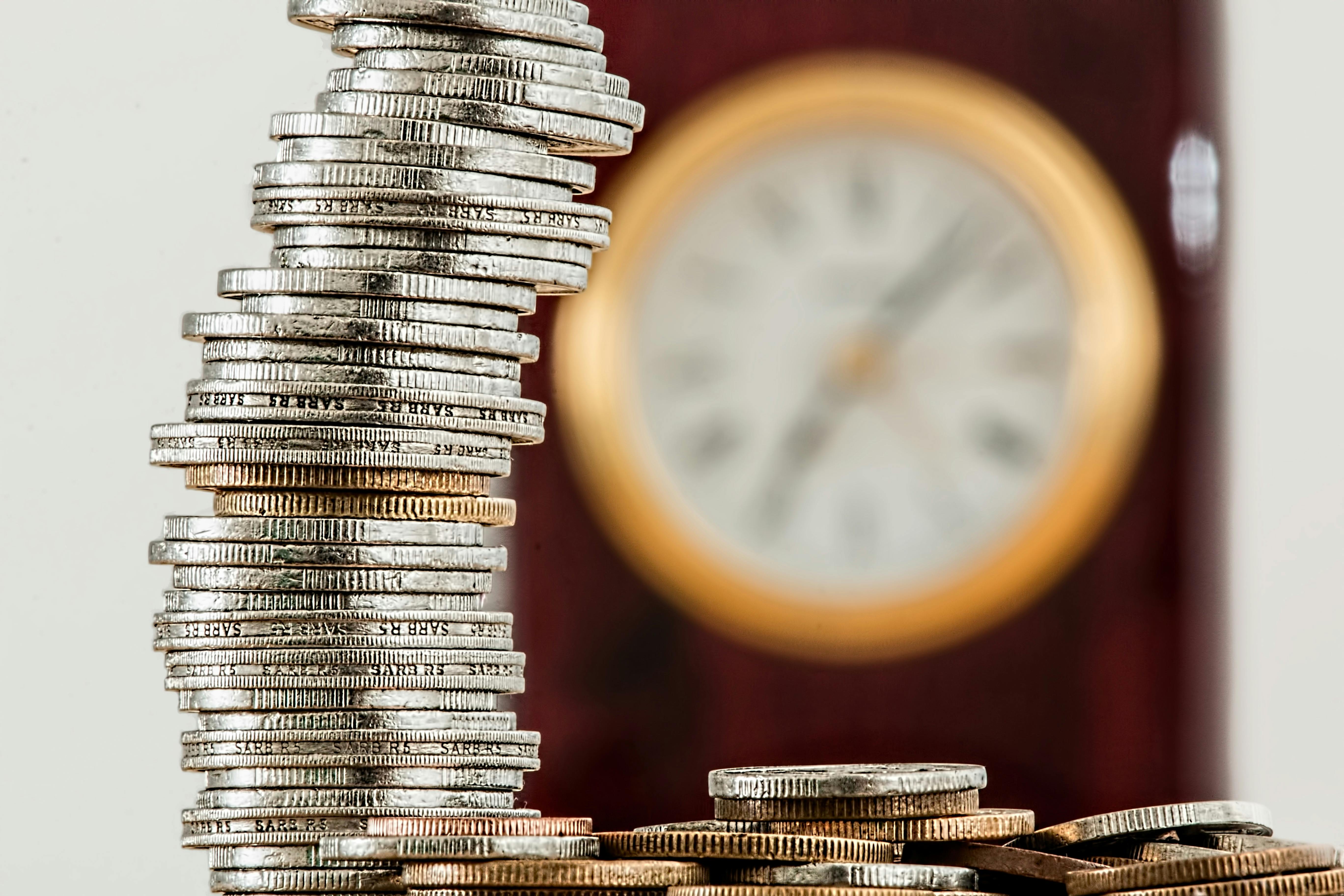 Stack of coins in front of blurred clock symbolizing time and money